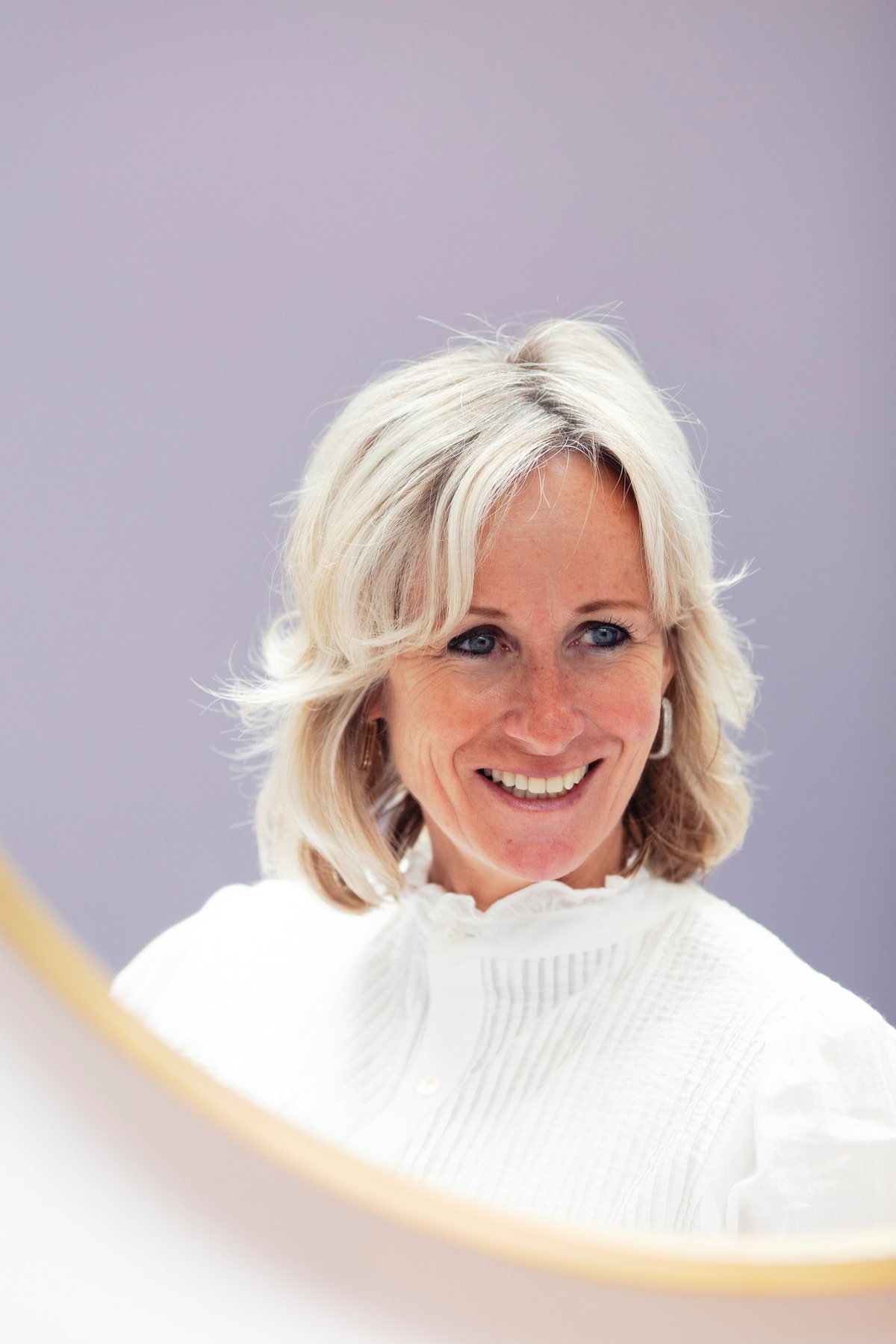 Evelien, eigenaresse van De Kapper, gespiegeld in de ronde gouden spiegel van haar salon
