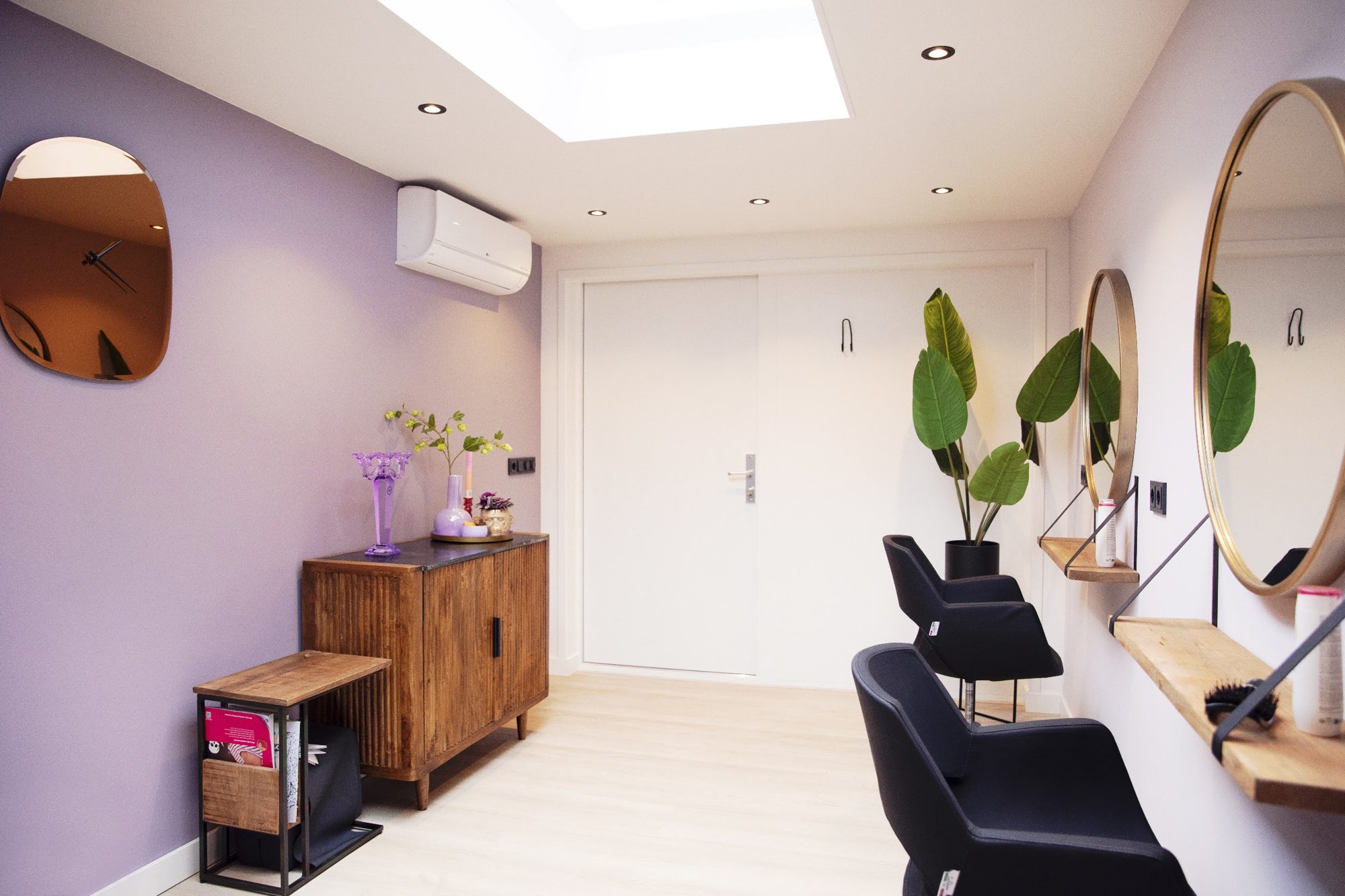 De salon van achteren gezien: lila muur, een amberkleurige spiegel, een houten kastje en de stoelen voor de ronde spiegels